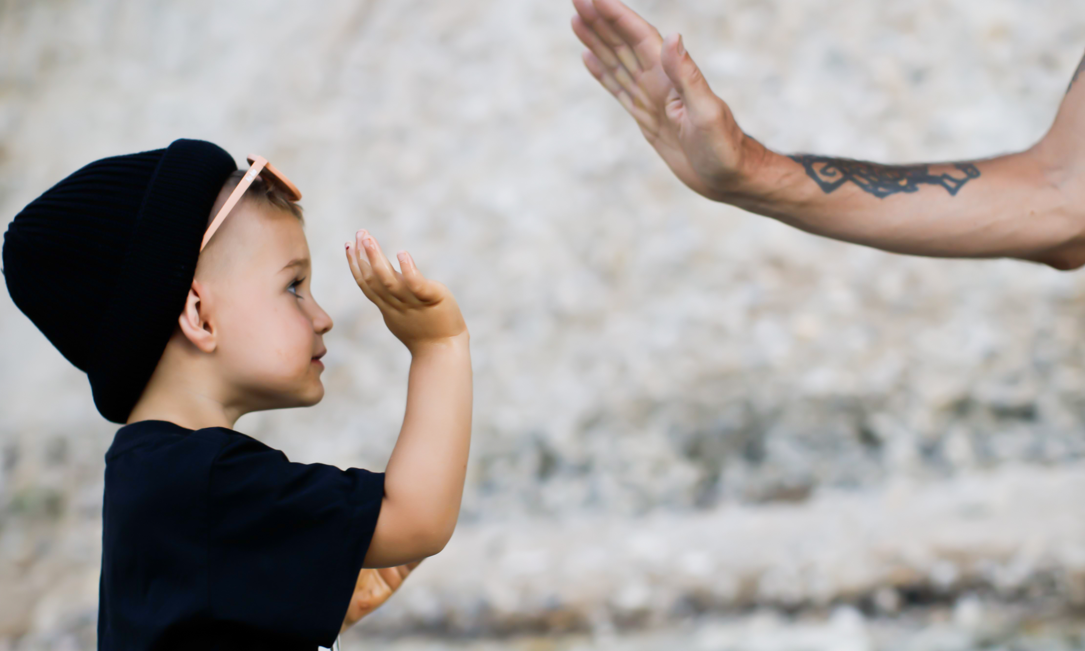 Kid wearing a black organic cotton beanie, unisex fit, outdoors giving high fives, enjoying eco-friendly fashion and playful moments.
