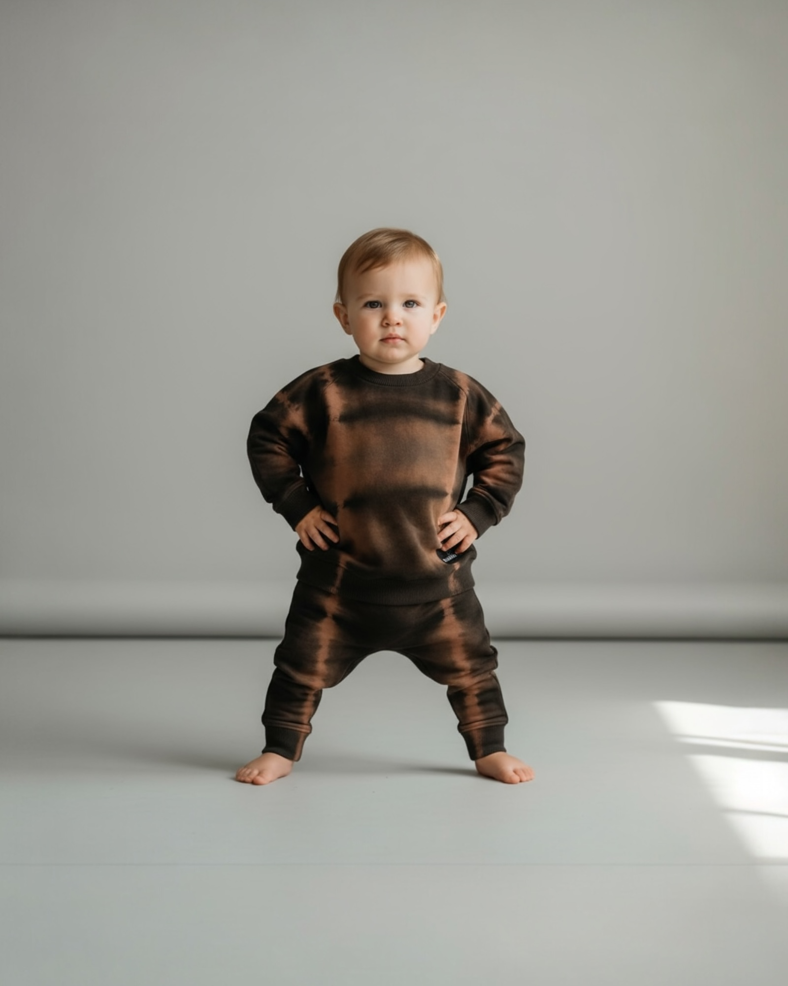 Child wearing a brown tie-dye outfit on a plain background