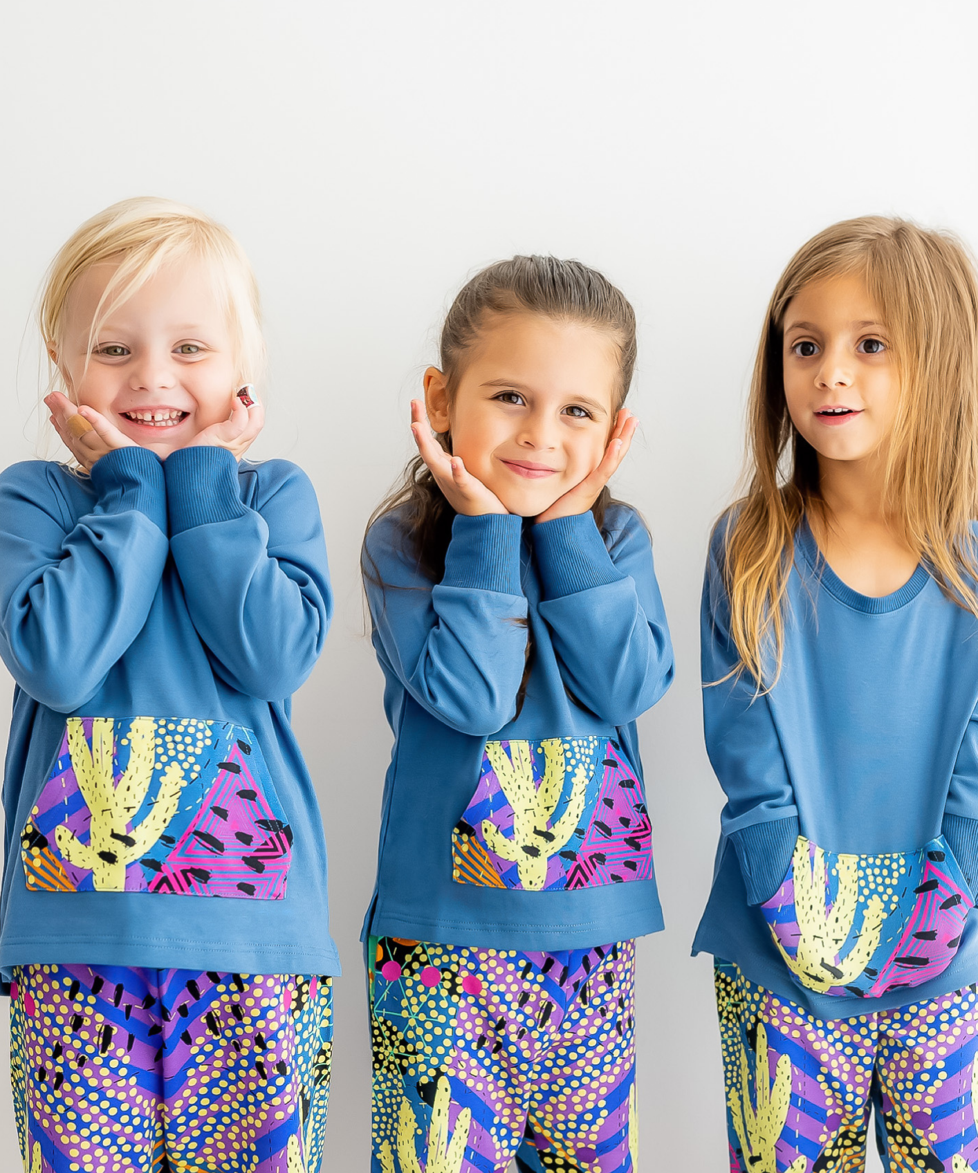 Three children posing in a two-piece kids loungewear set with a cactus print and harem pants.
