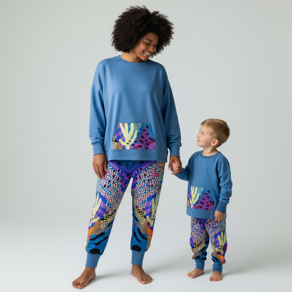 Woman and child wearing matching blue pajama sets with colorful patterns on a plain background