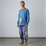 Man wearing a blue sweater and colorful pants with cactus  against a gray background