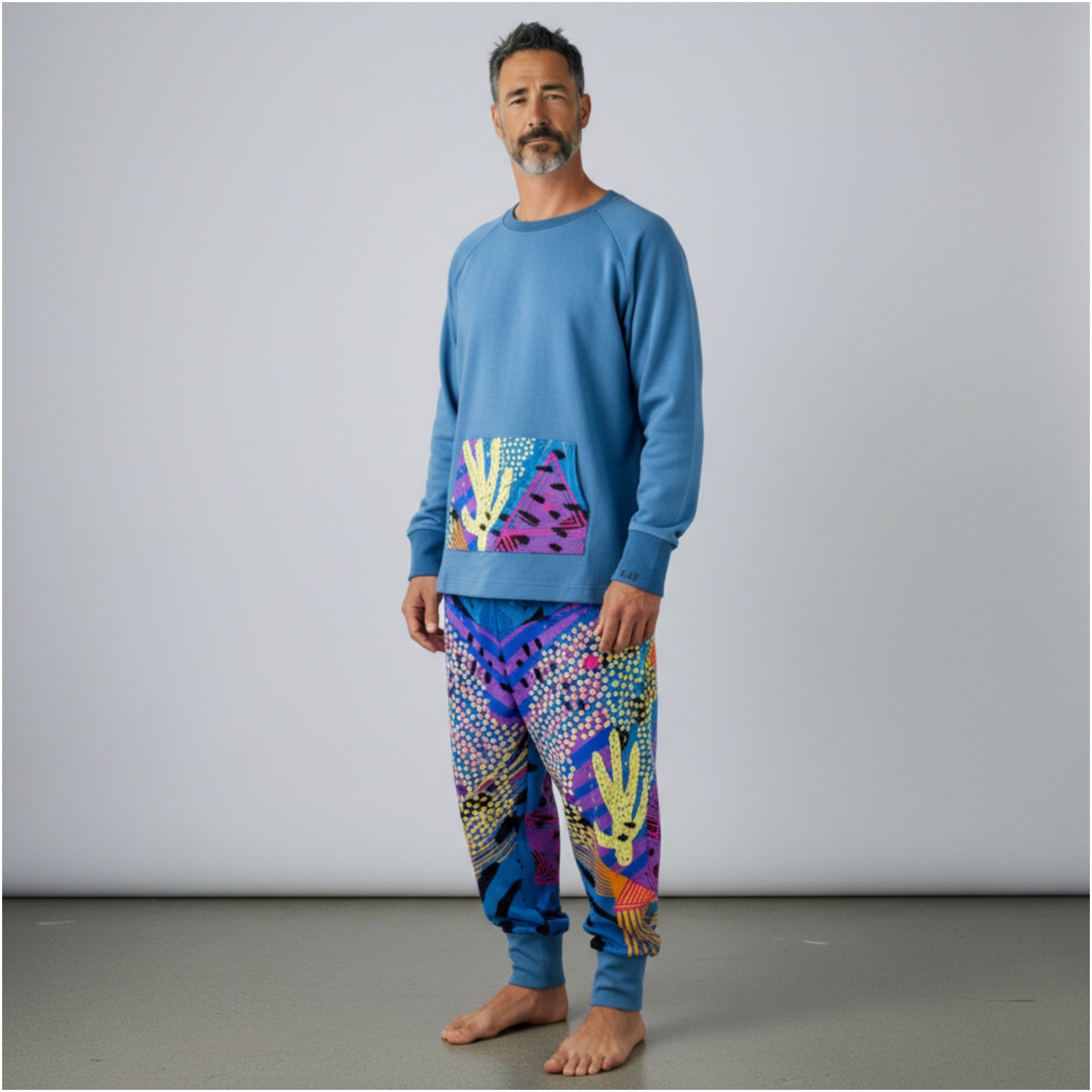 Man wearing a blue sweater and colorful pants with cactus  against a gray background