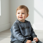 Child wearing a gray sweatshirt sitting on a light-colored floor with a neutral background